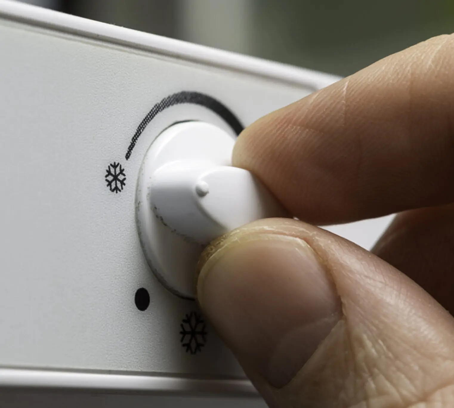Hand adjusting refrigerator temperature control dial.