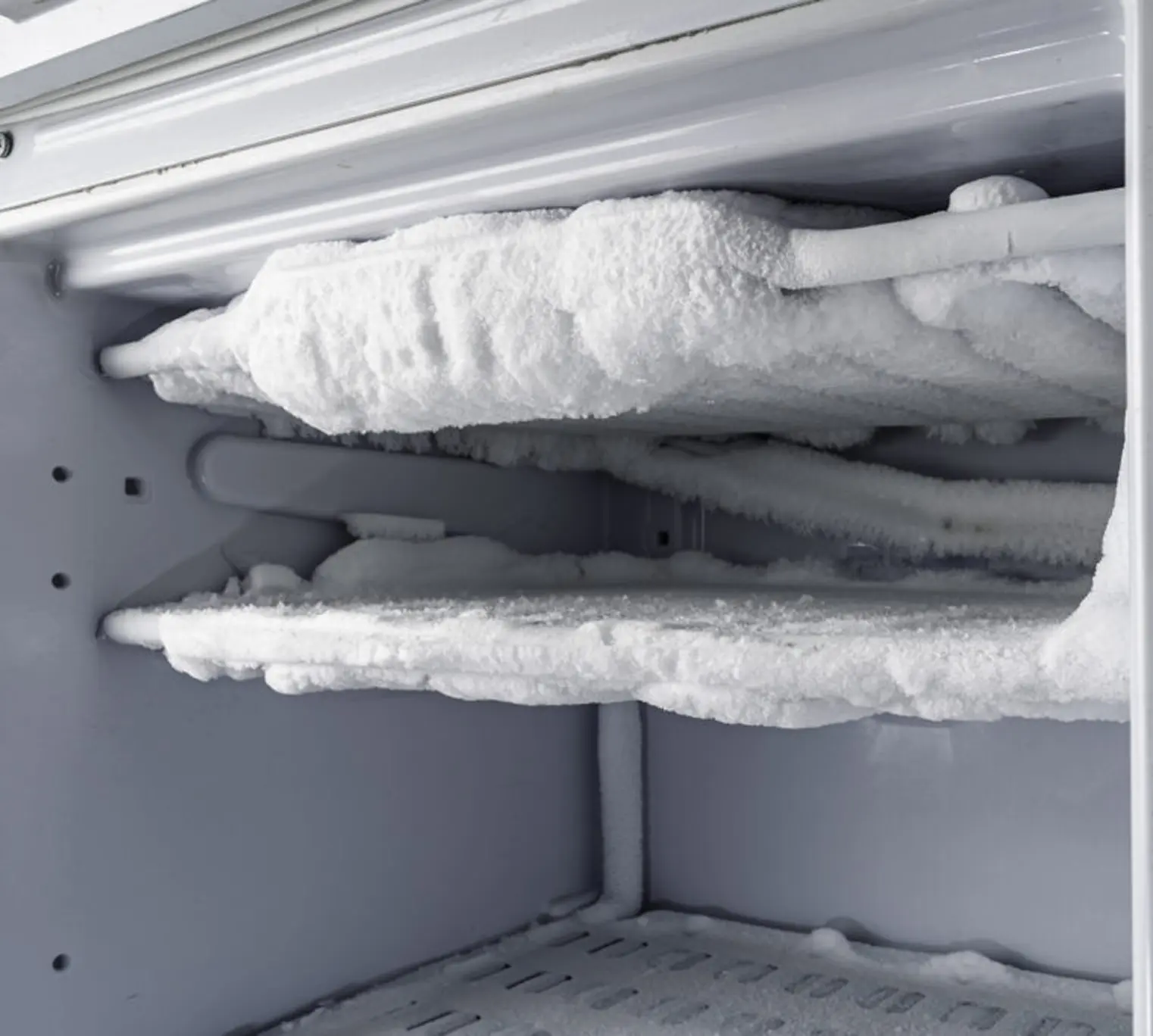 Heavy frost buildup inside freezer compartment on cooling coils.