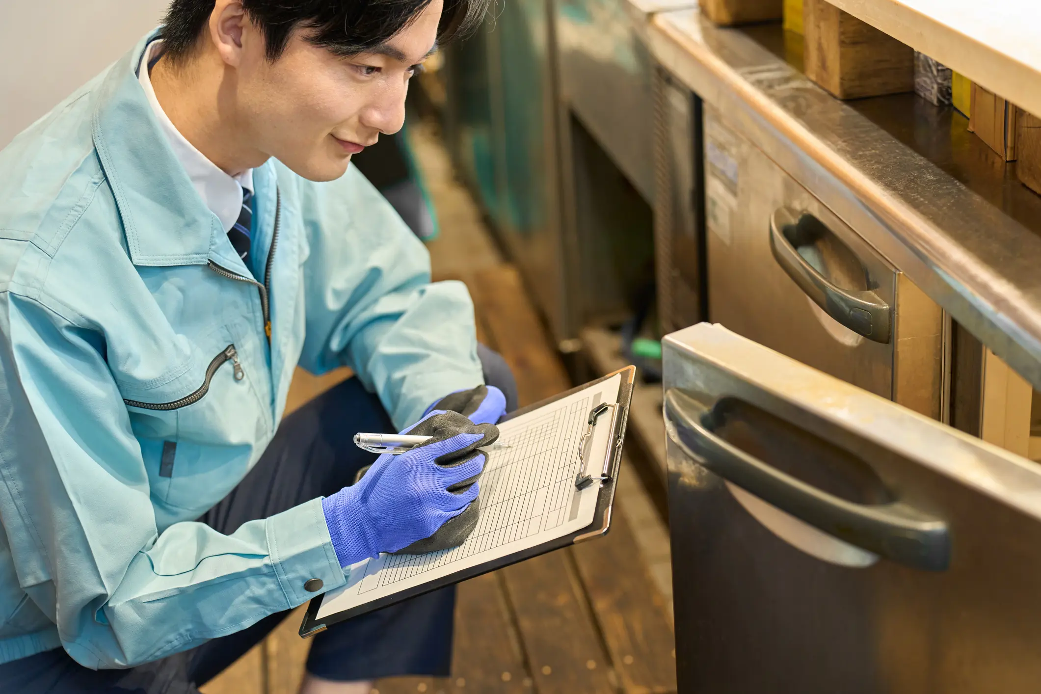 Appliance repair technician inspecting dishwasher and writing notes on clipboard.