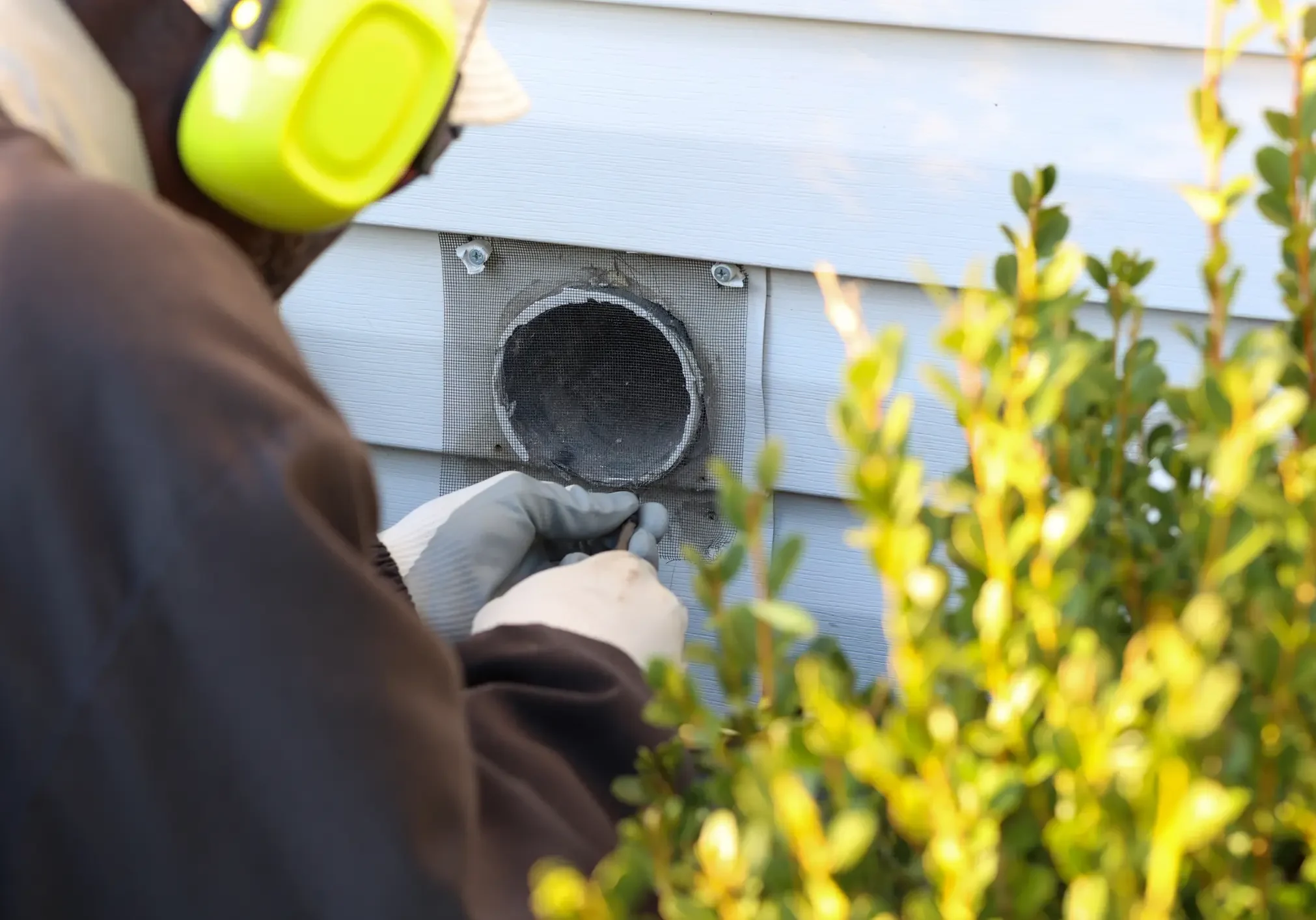 Technician cleaning exterior dryer vent on residential home.
